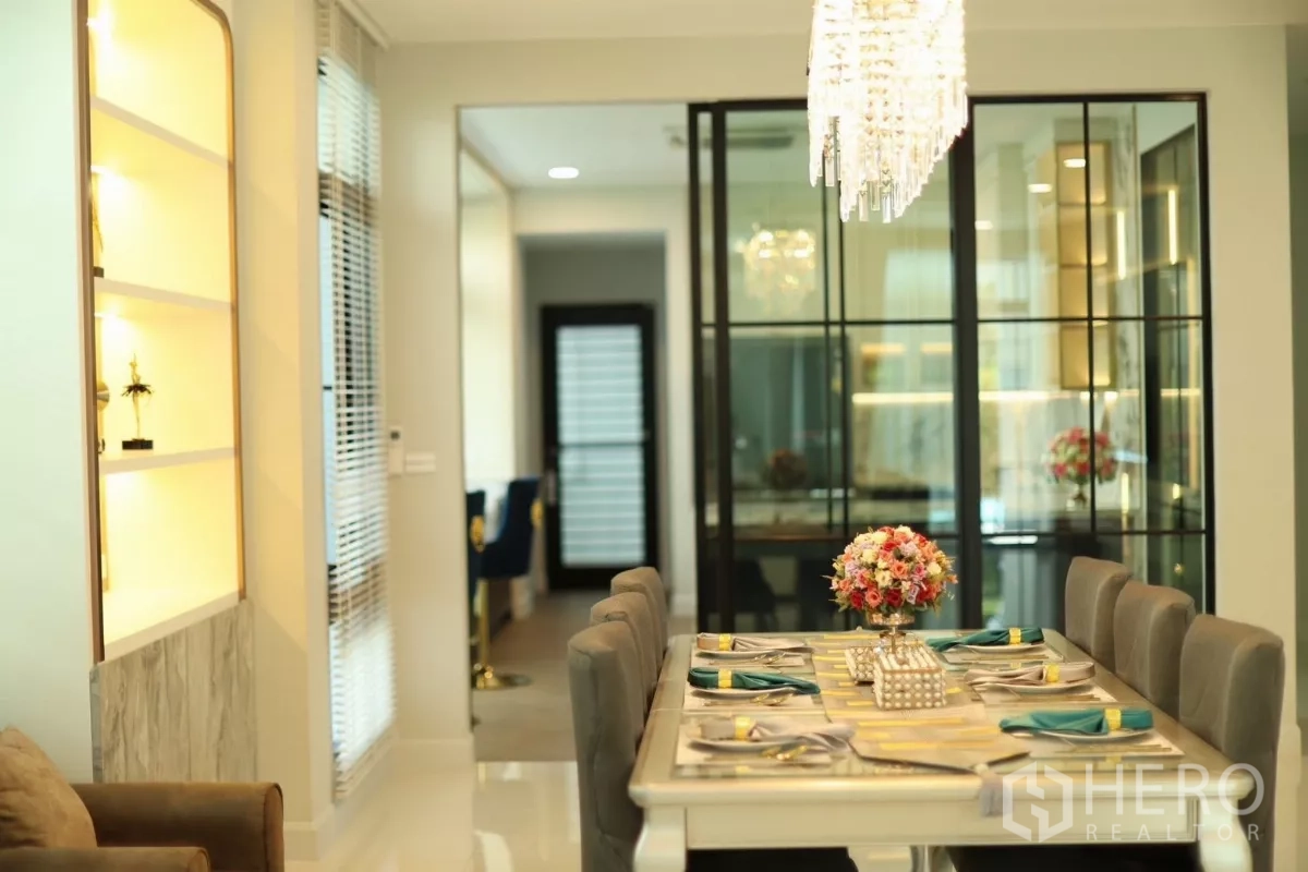 Detached House for rent or sale in Saphan Sung, Bangkok - Formal dining table set beneath chandelier, next to black-framed glass partition.