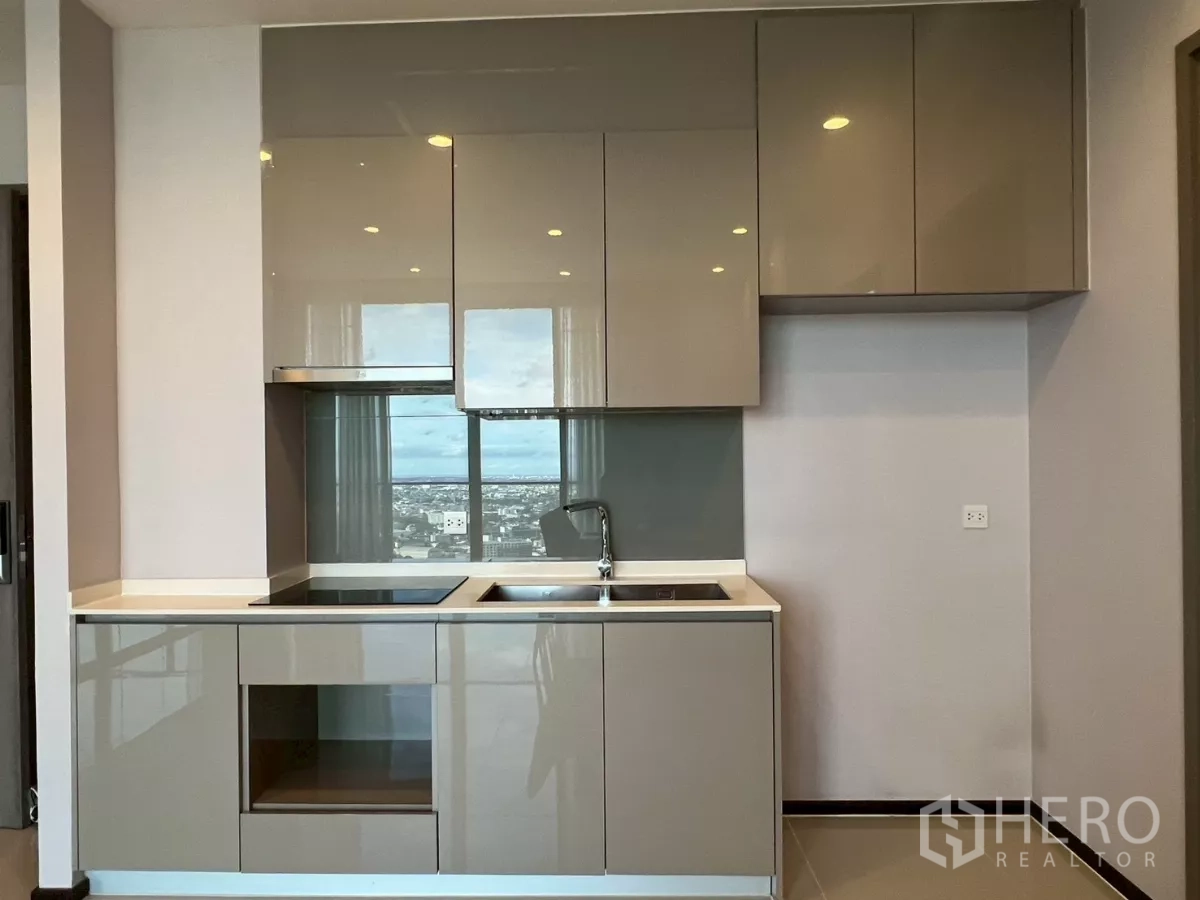 Condominium for rent in Phra Khanong, Bangkok - Compact modern kitchenette with glossy cabinets, induction cooktop, and sink.