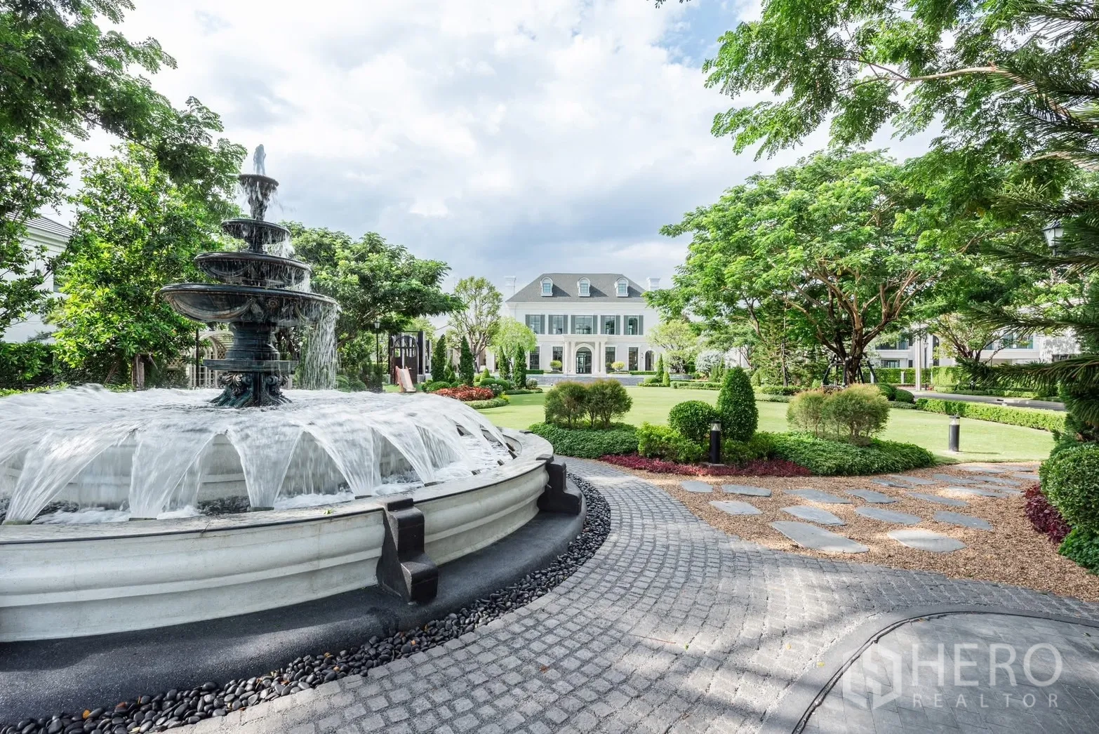 Detached House for rent or sale in Bang Phli, Samut Prakan - Tiered water fountain beside expansive landscaped gardens and a clubhouse facade.