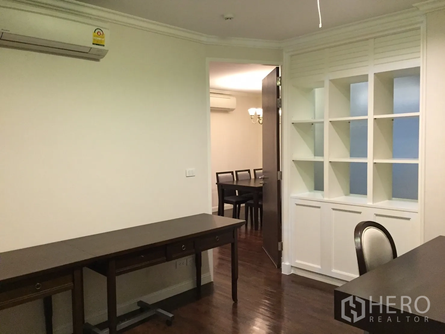 คอนโด ขายในHuai Khwang, Bangkok - มุมนั่งทำงานพร้อมโต๊ะไม้ยาวและตู้ชั้นบิวท์อินสีขาว เชื่อมต่อสู่โซนรับประทานอาหาร
