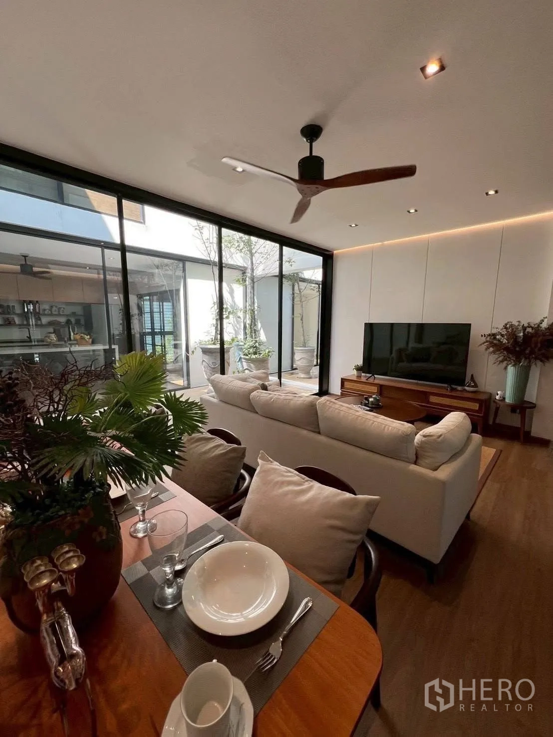 Home Office for rent or sale in Mueang Samut Prakan, Samut Prakan - Open-plan lounge with sofa, TV console and dining table facing a glass-walled courtyard.