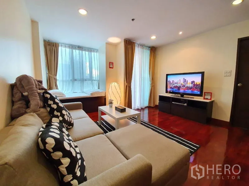Condominium for rent or sale in Pathum Wan, Bangkok - Lounge with sectional sofa facing a TV console, floor-to-ceiling windows and balcony door.