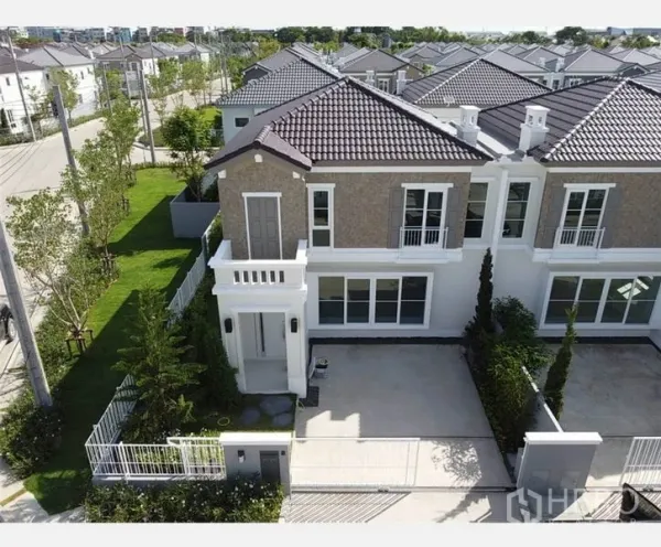 Townhouse for rent in Prawet, Bangkok - Aerial view of a modern two-storey corner townhouse with tiled roof, gated driveway and landscaped garden in a quiet estate.