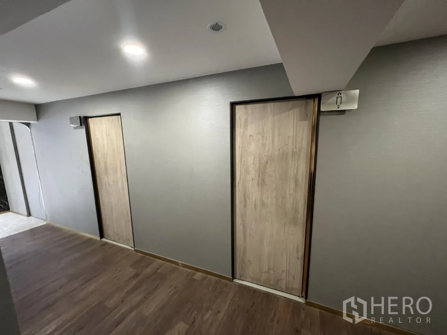 店屋 出租在Phra Khanong, Bangkok - 走廊设有两间洗手间门与木纹地，在筒灯照明下。