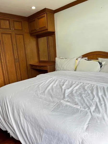 Condominium for rent in Ratchathewi, Bangkok - Cozy bedroom with white bedding and extensive built-in wooden wardrobes and a small desk.