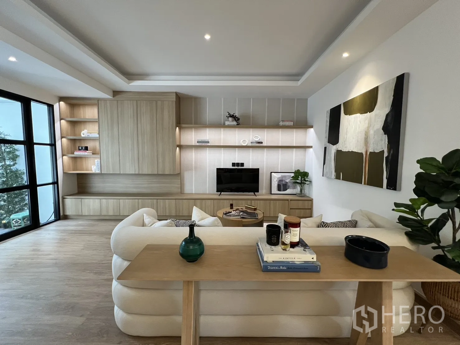 Townhouse for sale in Watthana, Bangkok - Contemporary living room with built-in wood shelving and a cozy cream sofa.