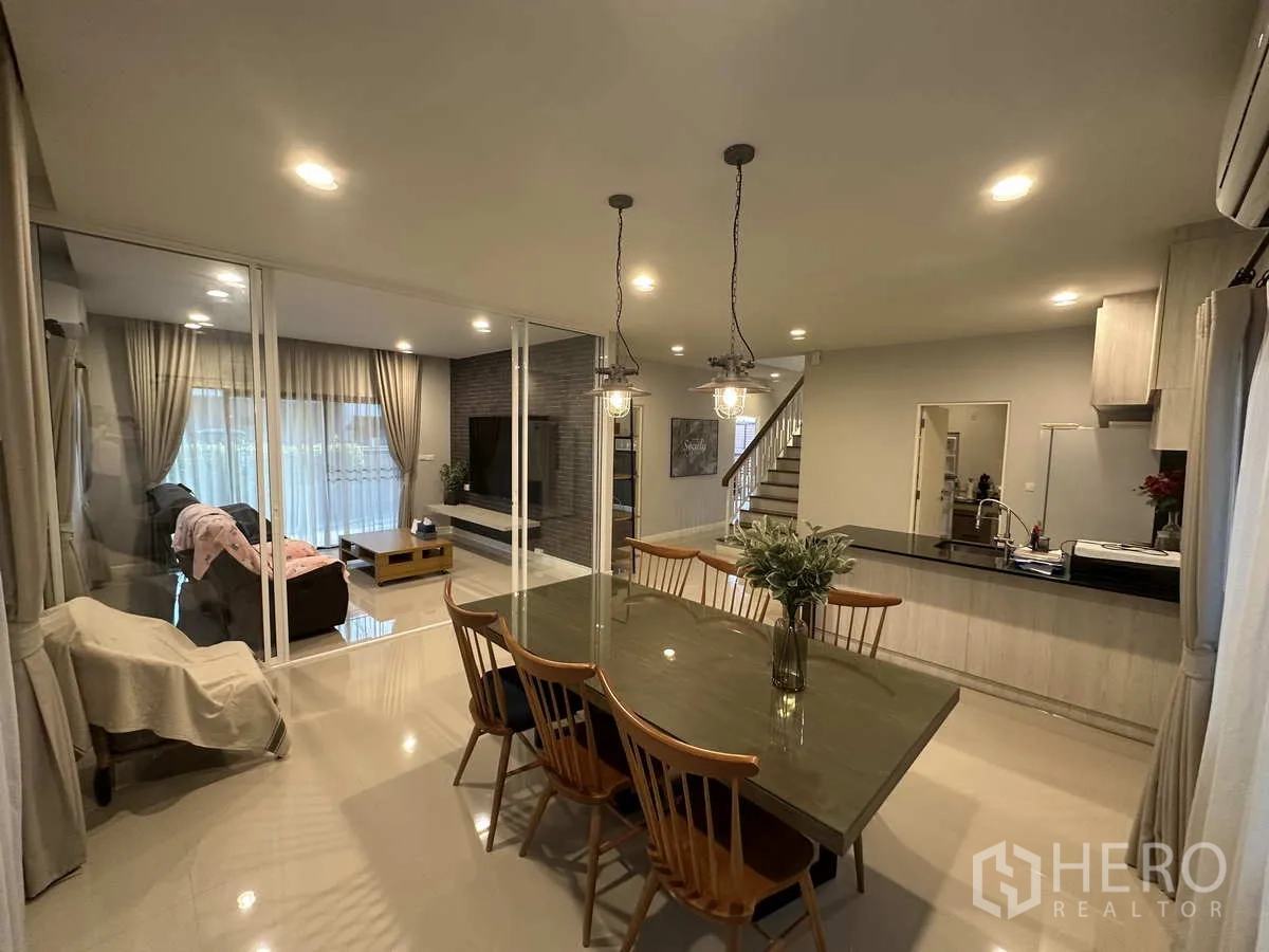 บ้าน ให้เช่าหรือขายในLam Luk Ka, Pathum Thani - ห้องทานอาหารกว้าง โคมไฟห้อย มองเห็นโซนนั่งเล่นผ่านผนังกระจก.