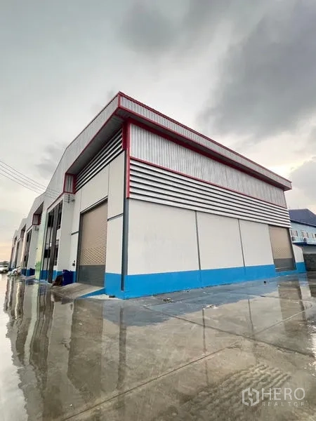 คลังสินค้า ให้เช่าในBang Phli, Samut Prakan - มุมมองด้านข้างโกดังพร้อมประตูม้วนและลานคอนกรีตเปียกฝน