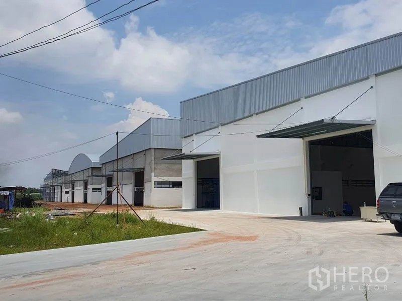 คลังสินค้า ให้เช่าในChon Buri - ด้านหน้าอาคารโกดังใหม่ในชลบุรี มีช่องขนถ่ายหลายจุด หลังคาทรงจั่วสูง และที่จอดรถใต้ท้องฟ้าโปร่ง