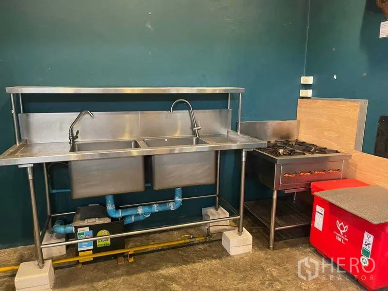 零售空间 出租在Khlong Toei, Bangkok - 不锈钢双槽水池与水龙头，旁为燃气灶，管线与电源插座齐全，深绿色墙面。