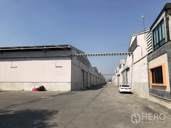 Warehouse for rent in Bang Bua Thong, Nonthaburi - Industrial lane lined with multiple warehouse units and a parked car.