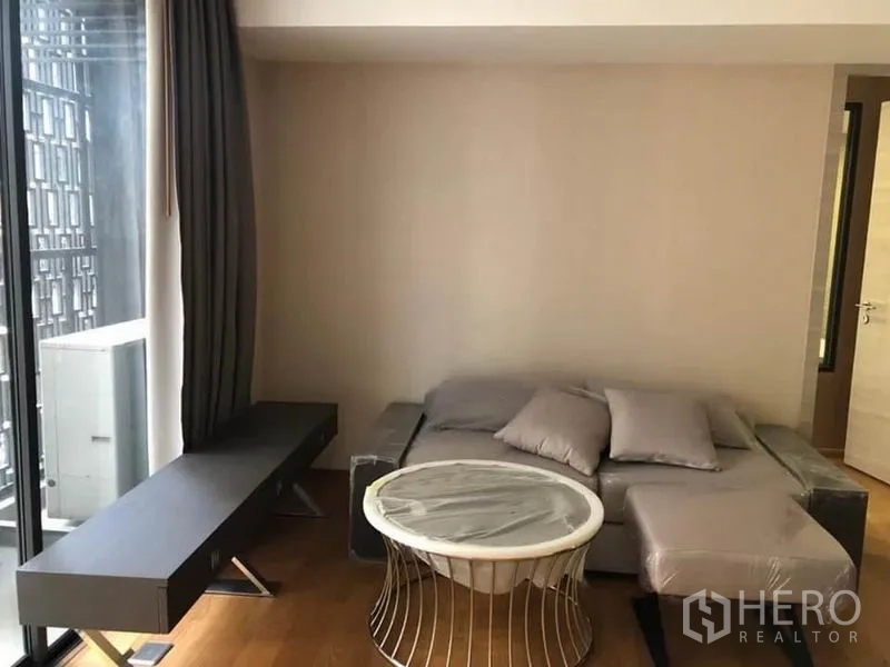 Condominium for rent in Pathum Wan, Bangkok - Cozy living room with gray sofa, round coffee table and floor-to-ceiling window with curtains.