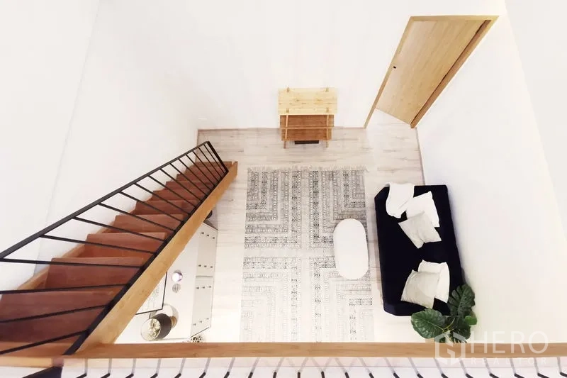 联排别墅 出租在Khlong Toei, Bangkok - 从夹层俯瞰客厅，可见沙发、图案地毯与楼梯。