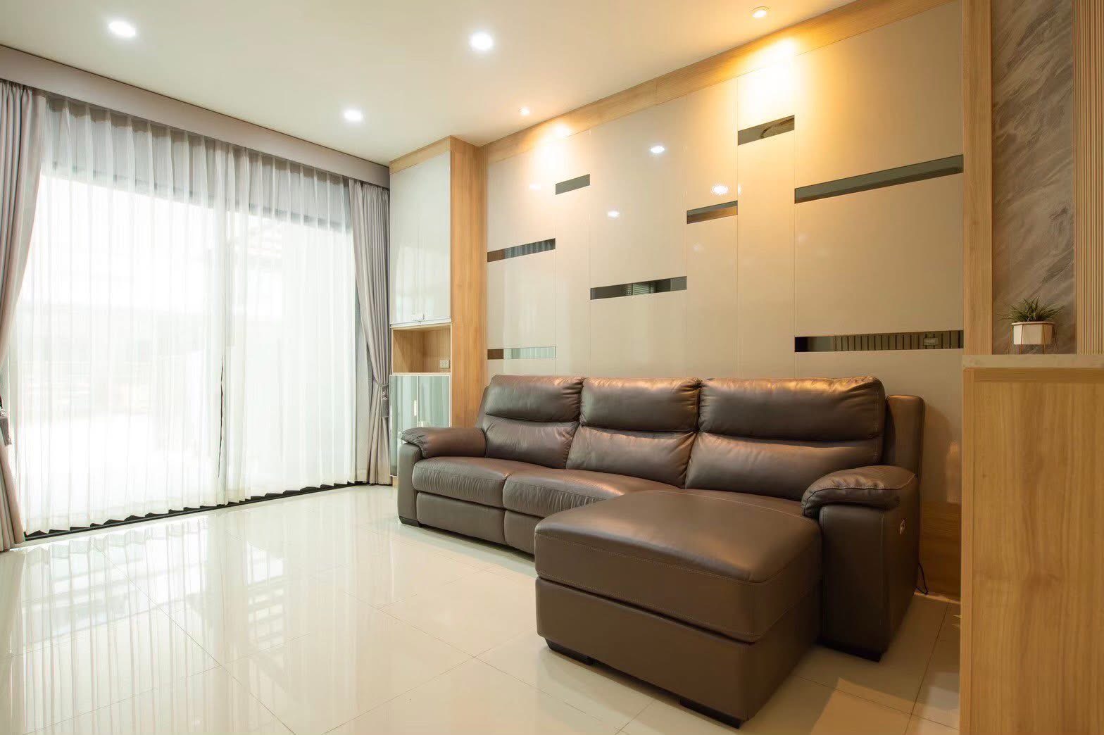 联排别墅 出租或出售在Lat Phrao, Bangkok - 宽敞客厅，大型皮沙发、亮面装饰墙与落地窗帘。