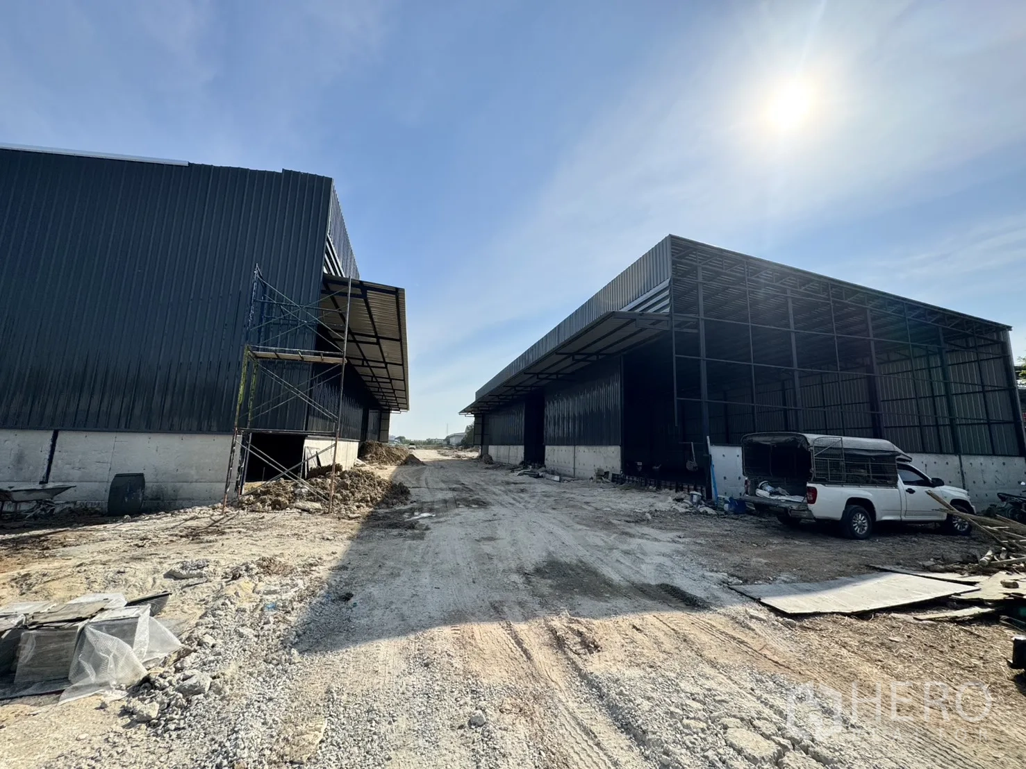 Warehouse for rent in Lam Luk Ka, Pathum Thani - Construction site view of steel‑frame warehouses with open fronts and a service vehicle.