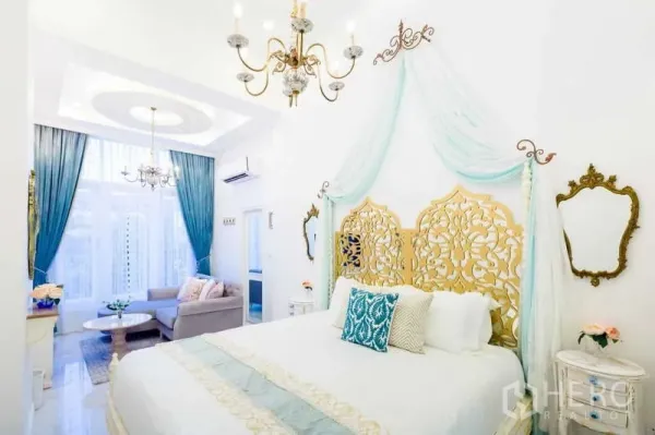 联排别墅 出租在Lat Phrao, Bangkok - 主卧配金色雕花床头、纱幔吊顶、水晶吊灯及窗边会客区