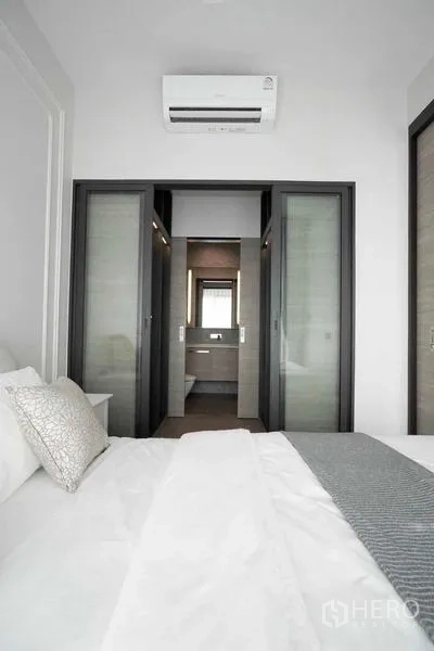 คอนโด ให้เช่า - มุมมองจากห้องนอนไปยังห้องน้ำในตัวผ่านประตูกระจกบานเลื่อนพร้อมแอร์.