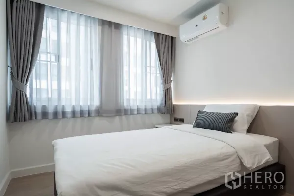 Apartment for rent - Cozy bedroom with double bed, large windows with gray curtains and a wall-mounted air conditioner.