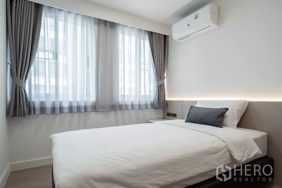 Apartment for rent - Cozy bedroom with double bed, large windows with gray curtains and a wall-mounted air conditioner.