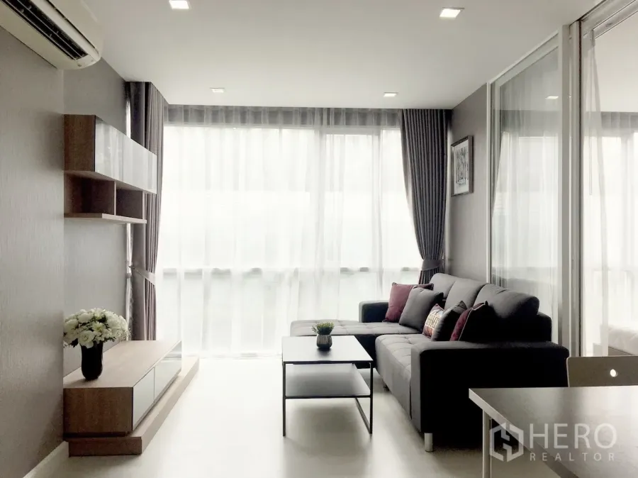 คอนโด ขายในPhra Khanong, Bangkok - ห้องนั่งเล่นสว่าง หน้าต่างสูงจรดเพดาน โซฟาเข้ามุม ชั้นวางบิวท์อิน และโต๊ะกลาง