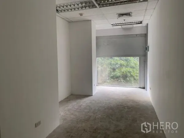 พื้นที่ขายปลีก ให้เช่า - พื้นที่ทรงลึก ผนังสีขาว ฝ้าทีบาร์ มีหน้าต่างด้านหลังรับแสงธรรมชาติและเห็นวิวต้นไม้