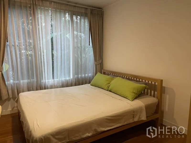 Condominium for rent in Pathum Wan, Bangkok - Cozy bedroom with double bed, sheer curtains and a large window overlooking garden greenery.