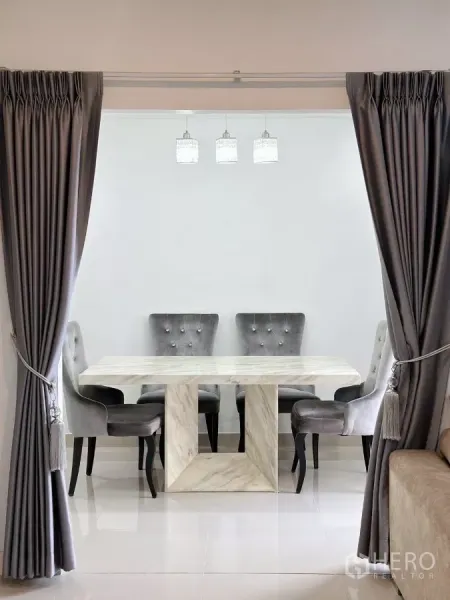 Townhouse for rent in Bang Phli, Samut Prakan - Dining area with a marble table and upholstered chairs framed by full-length drapes.