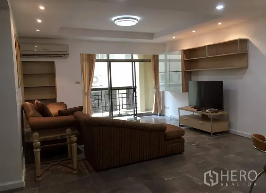 คอนโด ให้เช่าหรือขายในWatthana, Bangkok - ห้องนั่งเล่นกว้าง โซฟา L‑shape ชั้นวางทีวีและชั้นบิวท์อิน พร้อมประตูกระจกสไลด์ออกสู่ระเบียง