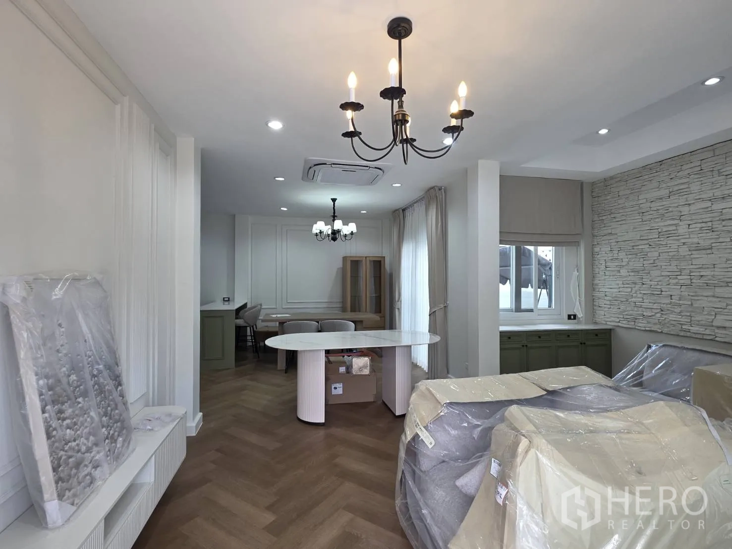 Detached House for sale in Lam Luk Ka, Pathum Thani - Living area with two chandeliers, paneled walls, stone accent, and wrapped furniture.