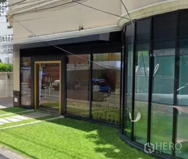 พื้นที่ขายปลีก ให้เช่าในWatthana, Bangkok - มุมใกล้ทางเข้าและกระจกโค้งโชว์หน้าร้าน รายล้อมด้วยสนามหญ้า