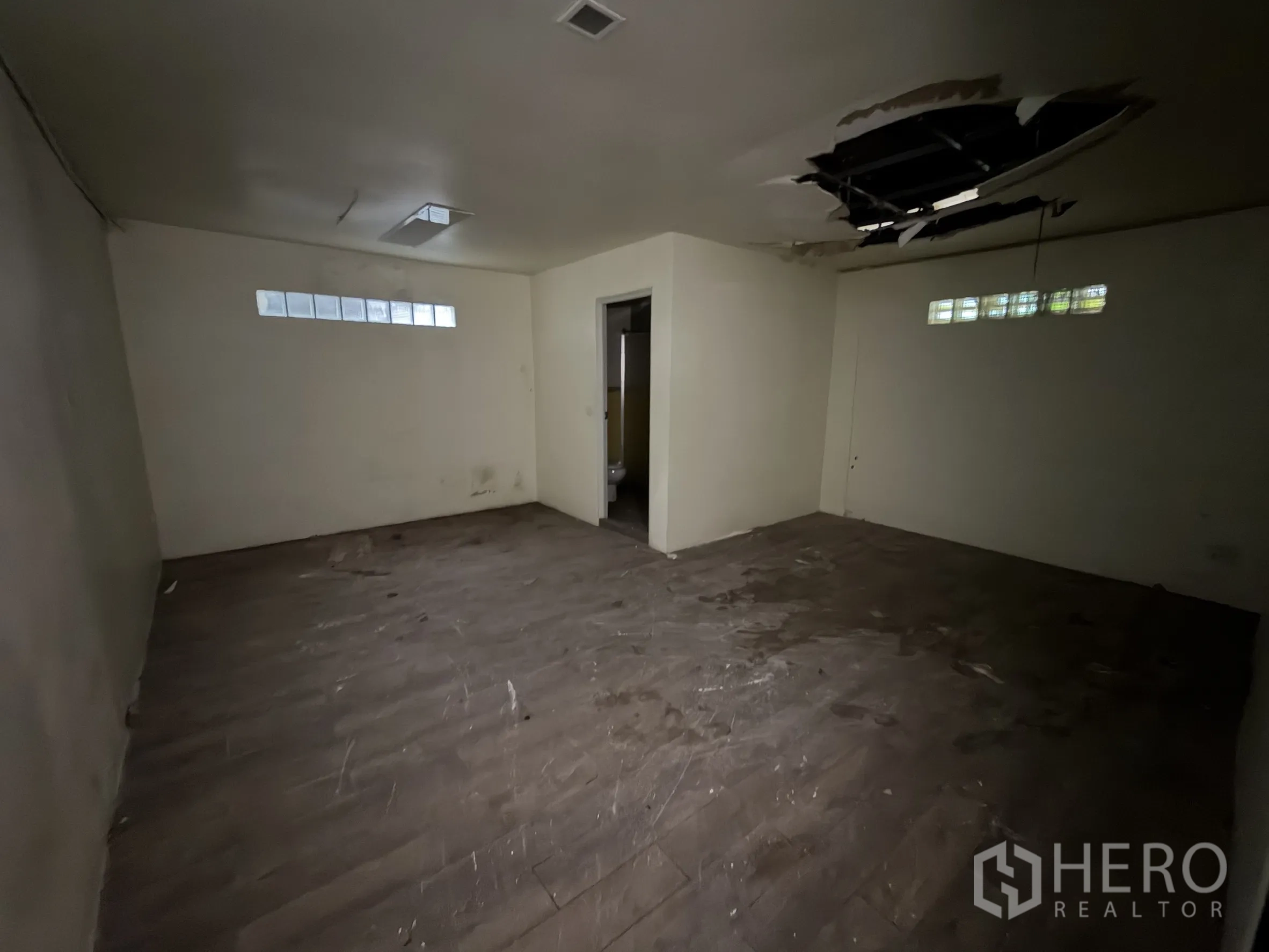 Shophouse for rent in Sathon, Bangkok - Spacious room with doorway to an ensuite and a section of damaged ceiling.