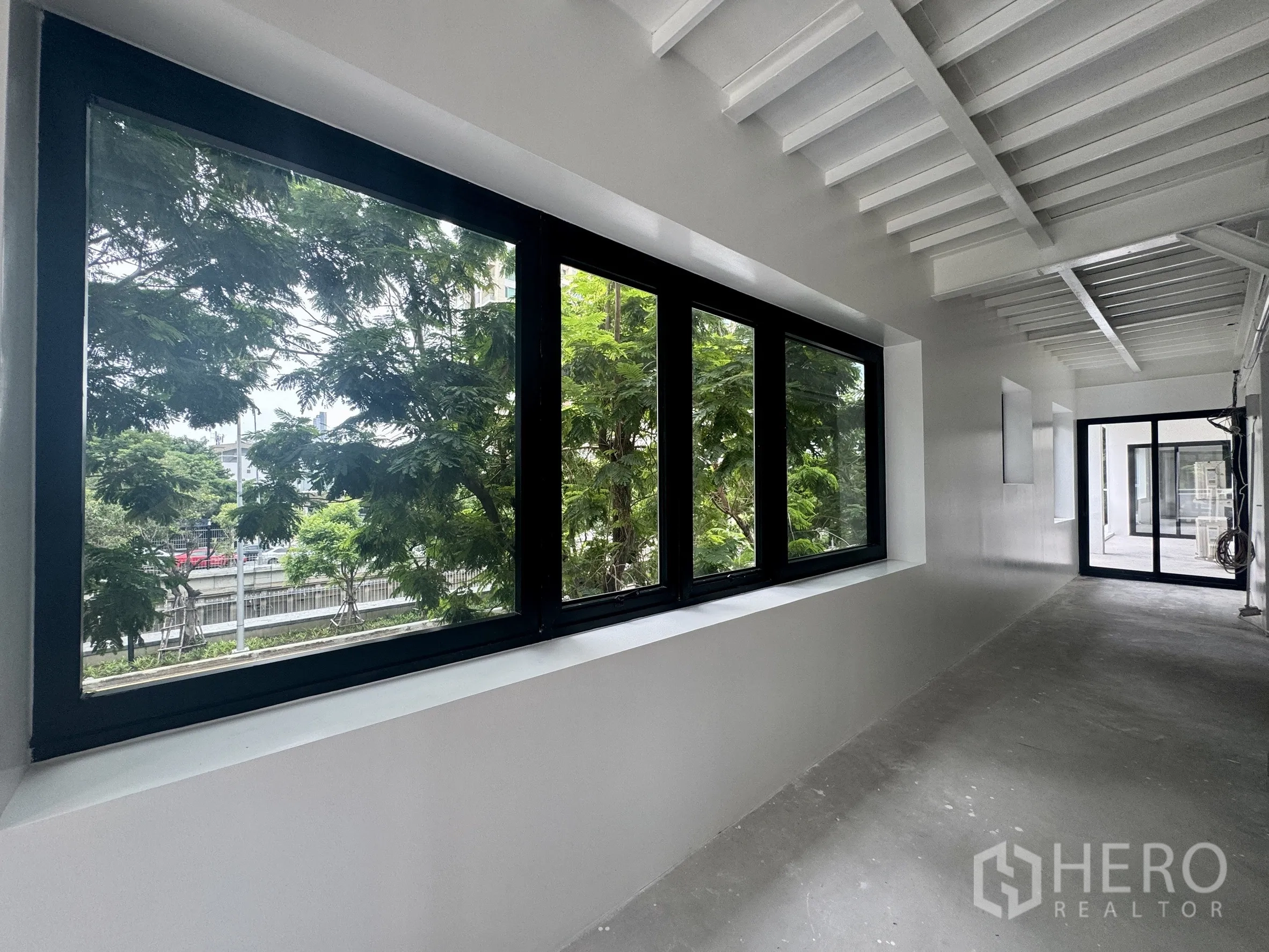 Office Space for rent in Sathon, Bangkok - Corridor with wide black-framed windows facing greenery and the city road.