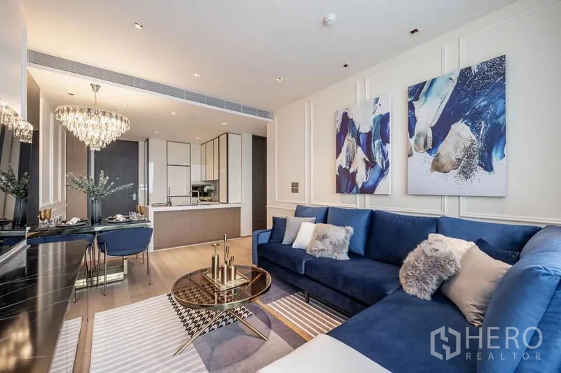 คอนโด ให้เช่าในPathum Wan, Bangkok - ห้องนั่งเล่นแบบเปิดโล่ง โซฟาสีน้ำเงิน ชุดทานอาหารพร้อมโคมระย้า และครัวสมัยใหม่