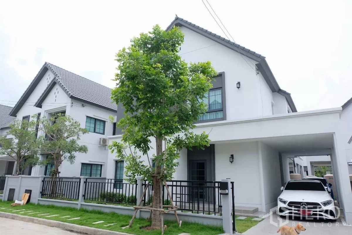Detached House for sale in Bang Phli, Samut Prakan - Modern two-storey detached house with carport, black fence, front lawn and shade trees on a quiet residential street