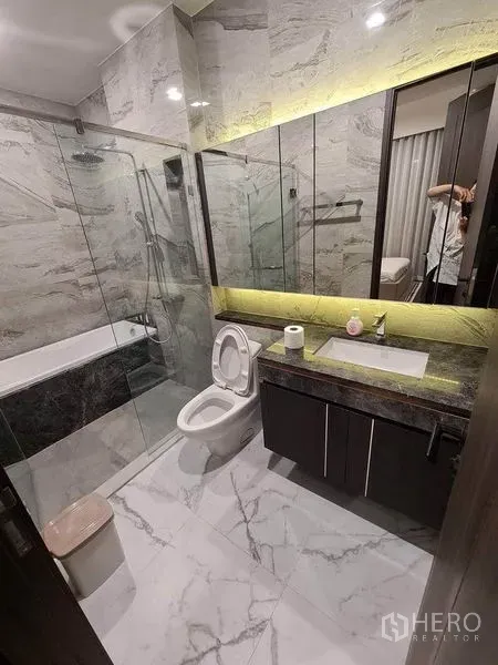 Condominium for rent in Watthana, Bangkok - Marble bathroom with glass shower, bathtub, and backlit mirror.