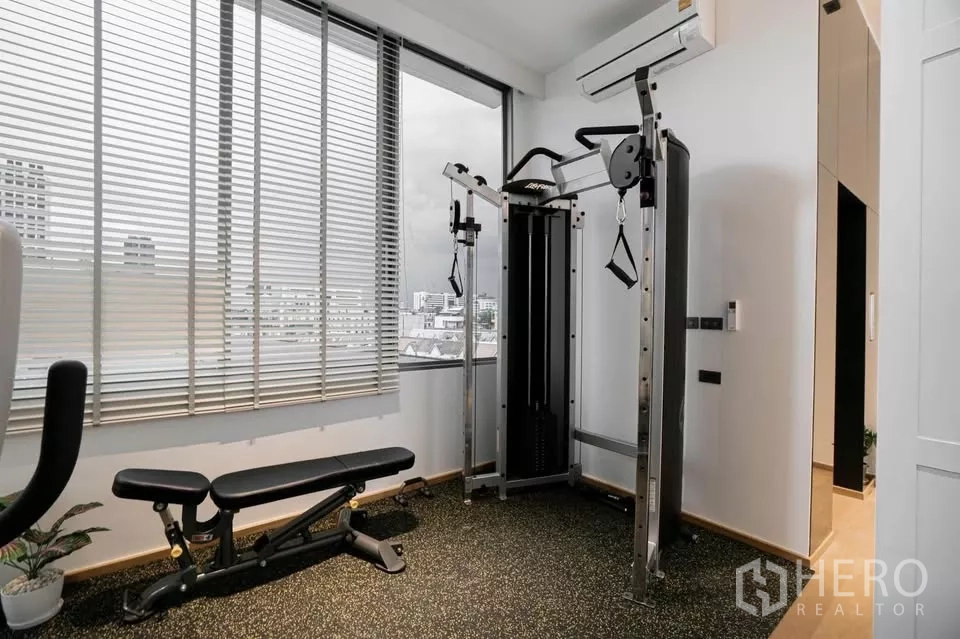 ทาวน์เฮาส์ ขายในChatuchak, Bangkok - ห้องฟิตเนสพร้อมม้านั่งออกกำลังกายและวิวเมืองผ่านมู่ลี่