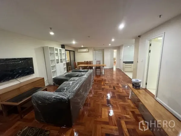 公寓 出租在Watthana, Bangkok - 开放式客餐厅，沙发、电视墙与书柜一体，铺设亮面拼花木地板。