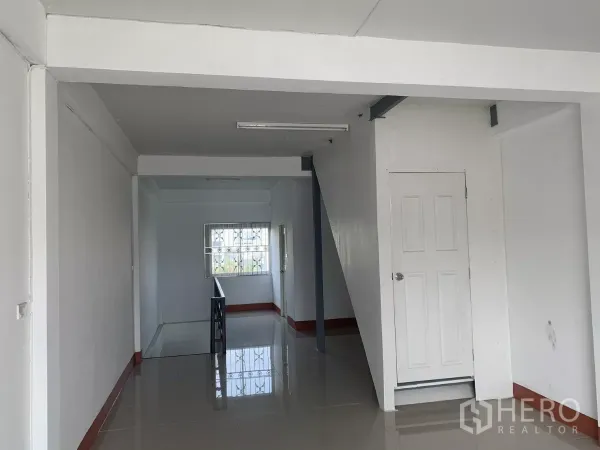 Home Office for rent in Lat Krabang, Bangkok - Upper‑floor corridor with glossy tiles, window with security bars and a white storage door.