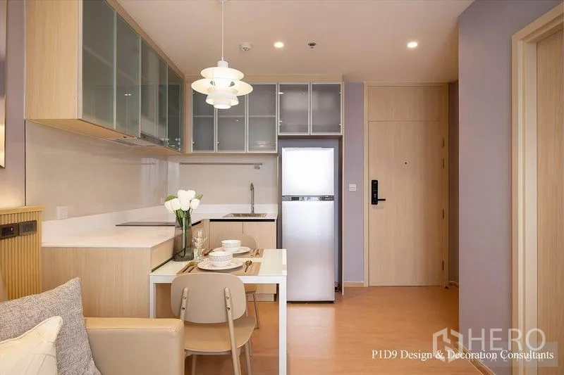 Condominium for rent in Watthana, Bangkok - Kitchen and entryway view with pendant over dining table, cooktop, sink and tall refrigerator.