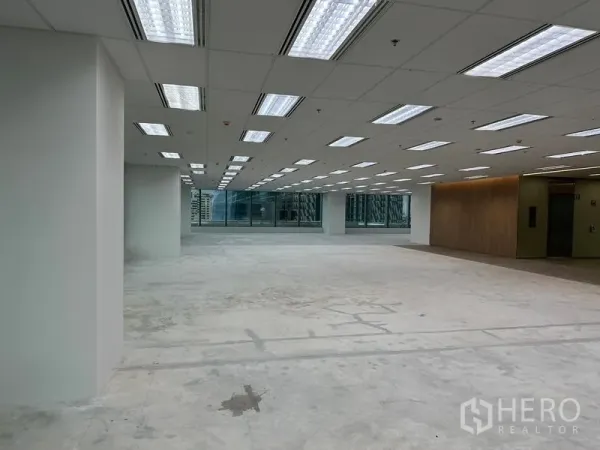 Office Space for rent in Ratchathewi, Bangkok - Open-plan office floor with grid ceiling lights, unfinished concrete slab, large windows and a wood-accent elevator lobby.