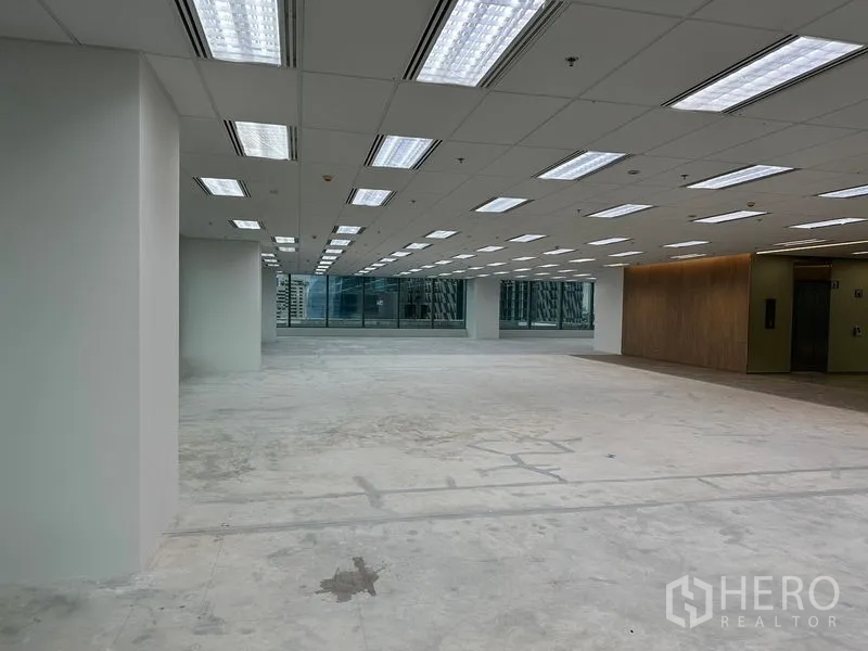 Office Space for rent in Ratchathewi, Bangkok - Open-plan office floor with grid ceiling lights, unfinished concrete slab, large windows and a wood-accent elevator lobby.
