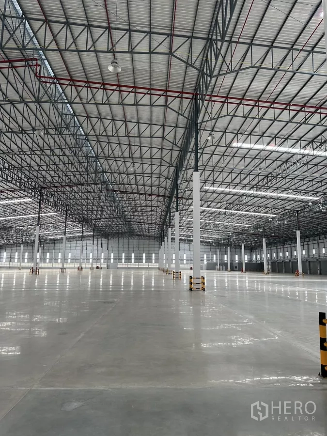 Factory for rent in Chon Buri - Expansive, clear-span warehouse hall with reflective concrete floor and side windows.