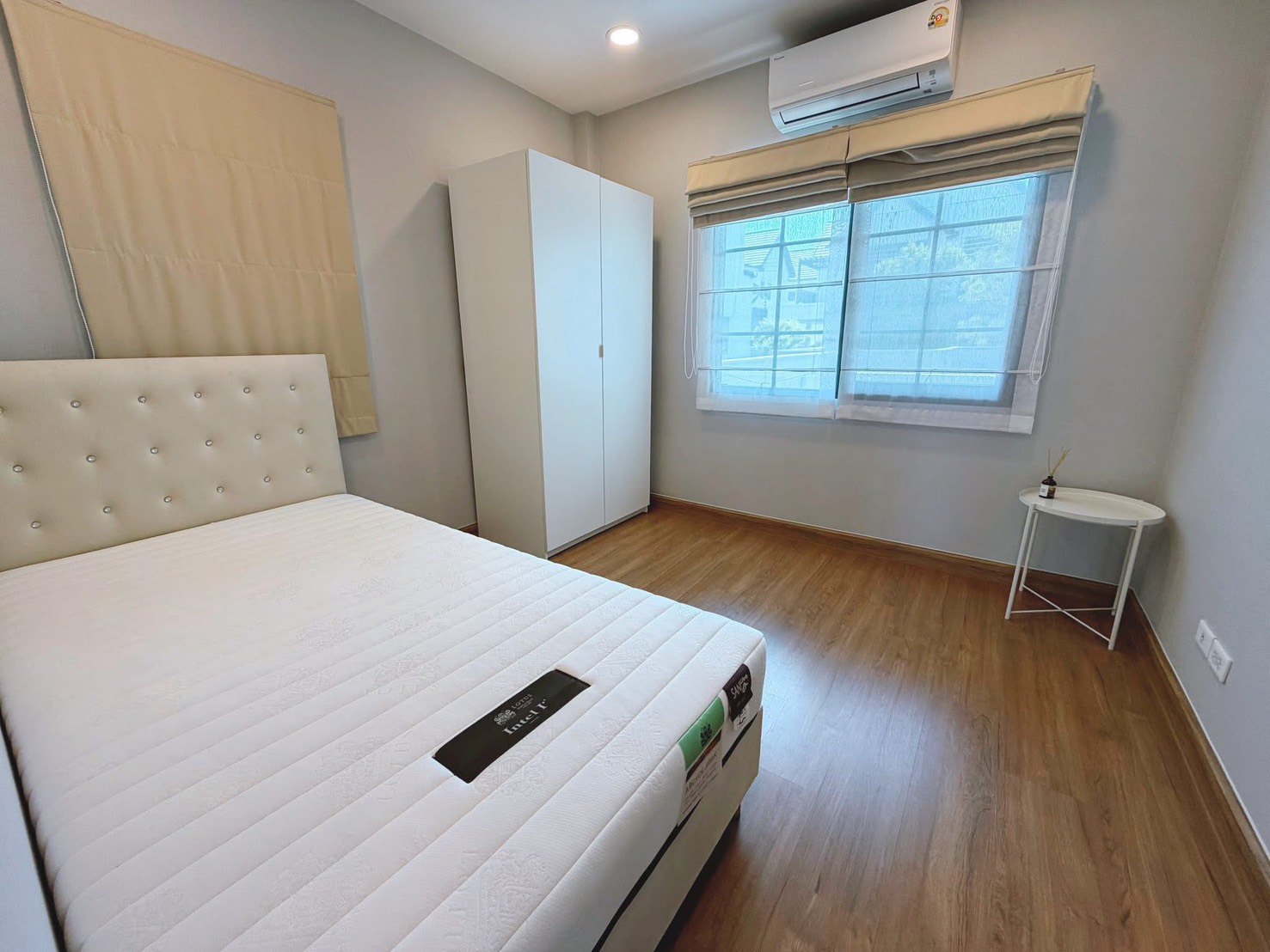 独立式住宅 出租在Bang Phli, Samut Prakan - 明亮卧室，白色软包床、衣柜、木地板、空调与窗帘窗户。