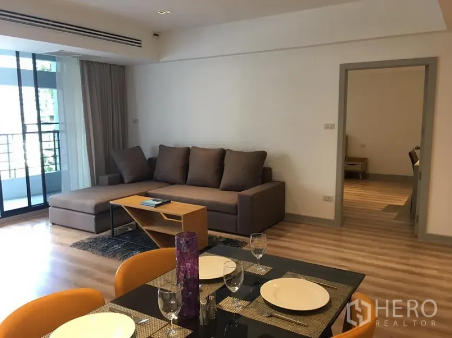 อพาร์ทเมนท์ ให้เช่าในKhlong Toei, Bangkok - ห้องนั่งเล่นสว่าง พื้นไม้ โซฟาเข้ามุม และประตูบานเลื่อนออกสู่ระเบียง