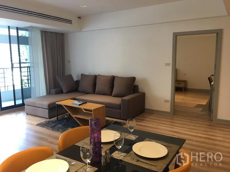 อพาร์ทเมนท์ ให้เช่าในKhlong Toei, Bangkok - ห้องนั่งเล่นสว่าง พื้นไม้ โซฟาเข้ามุม และประตูบานเลื่อนออกสู่ระเบียง