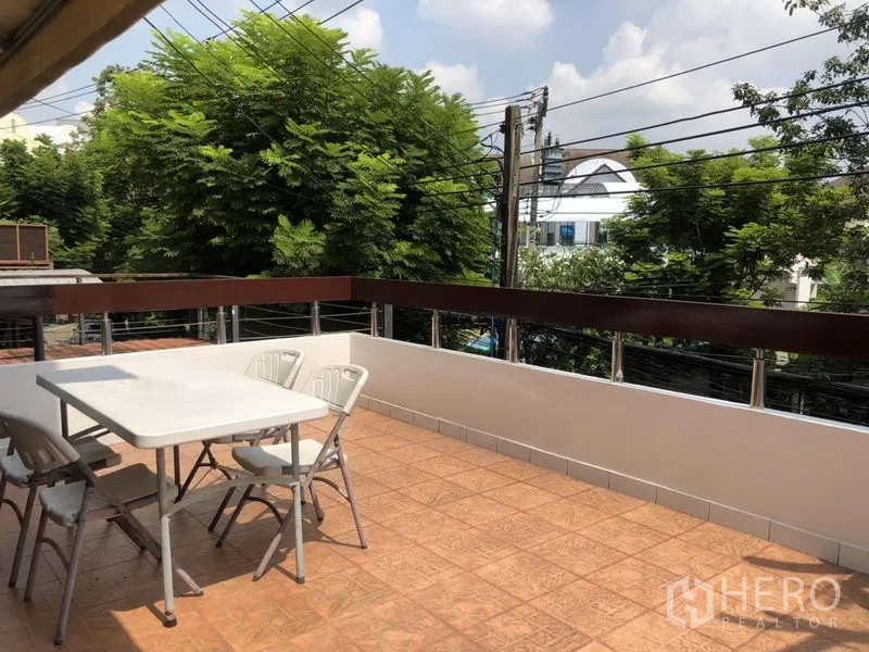 ทาวน์เฮาส์ ให้เช่าหรือขายในBangkok - เทอเรสปูกระเบื้องกว้าง โต๊ะพร้อมเก้าอี้ ราวกันตก และวิวต้นไม้รอบบ้าน