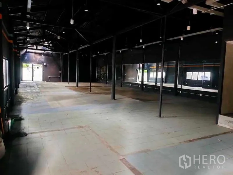 Warehouse for rent in Suan Luang, Bangkok - Open-plan storage hall with black ceiling, strip lighting and large windows leading to exit doors.