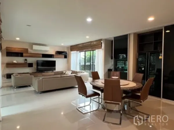 Detached House for rent or sale in Bang Kapi, Bangkok - Bright open-plan living and dining area with sectional sofa, TV wall and round dining table.