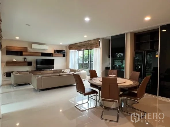 Detached House for rent or sale in Bang Kapi, Bangkok - Bright open-plan living and dining area with sectional sofa, TV wall and round dining table.