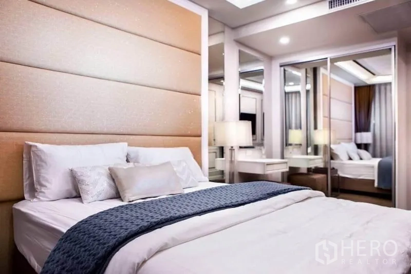 Condominium for rent in Huai Khwang, Bangkok - Cozy bedroom featuring a padded headboard, mirrored wardrobe and dressing table with soft lighting.